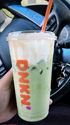 a person holding a drink in their hand while sitting in a car with the steering wheel behind them