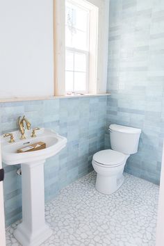 a white toilet sitting next to a bathroom sink under a window in a blue tiled room