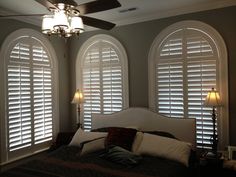 a bedroom with three arched windows and a bed in front of the window has pillows on it