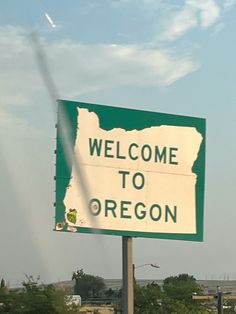 a welcome to oregon sign in front of a highway with trees and sky behind it