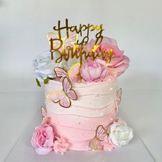 a birthday cake with pink and white flowers on it that has the words happy birthday spelled in gold