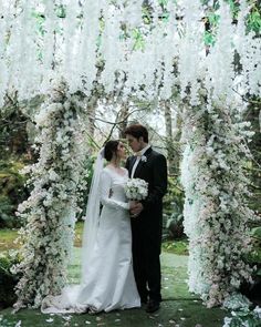 a bride and groom standing under an arch covered in flowers