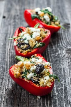 three stuffed red peppers with cheese and herbs in them sitting on a wooden table, ready to be eaten