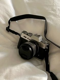 a black camera sitting on top of a white bed next to a strap that is attached to it