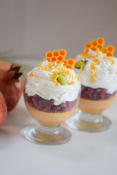 three desserts in small glass dishes on a white table with apples and pomegranates