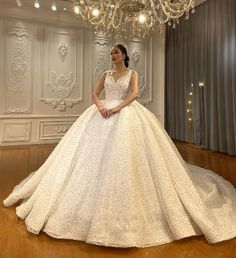 a woman in a wedding dress standing on a wooden floor with a chandelier