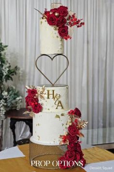 a three tiered wedding cake with red roses on top and the word h is spelled in gold