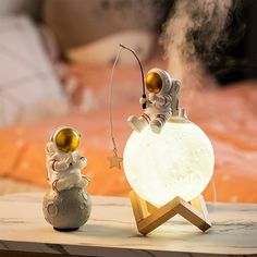 two small figurines sitting on top of a wooden table next to a lamp