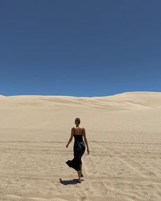 a woman walking across a sandy field under a blue sky