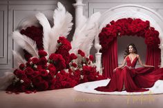 a woman in a long red dress sitting on a stage surrounded by roses and feathers