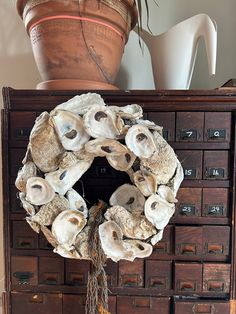 a wreath made out of seashells sits on an old dresser