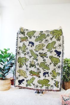 a blanket with green and blue frogs on it next to potted plants in a room