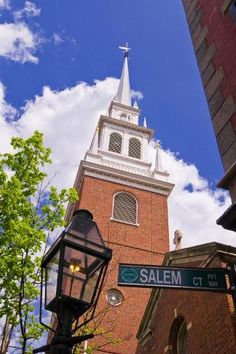 a tall brick building with a steeple and street signs in front of it on a sunny day