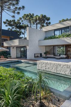 an outdoor swimming pool in front of a modern house with trees and plants around it