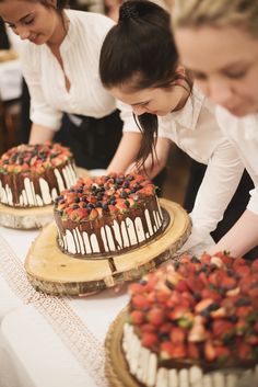 two women are decorating cakes with strawberries and chocolate frosting on the table