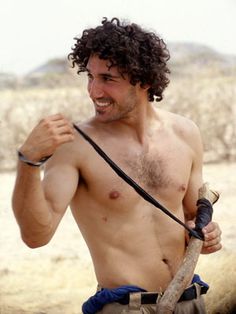 a shirtless man holding a stick in the desert