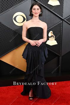 a woman in a black dress on the red carpet at an awards event, posing for a