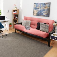 a living room with a futon couch, chair and computer on the desk in it