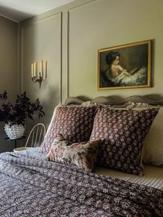 a bed with two pillows and a painting on the wall above it in a bedroom