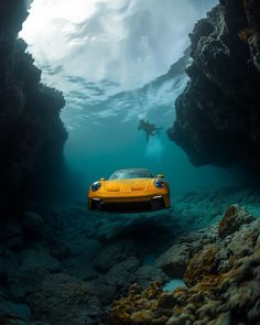 a yellow sports car is underwater in the ocean with rocks and water around it, while a man swims by