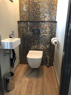 a bathroom with a toilet, sink and trash can on the floor in front of a tiled wall