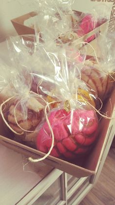 some pink and yellow pastries in a box on a table with plastic wrap around them