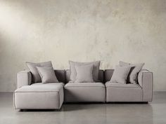 a white couch with pillows on it in front of a concrete wall and flooring