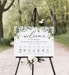 a welcome sign with greenery and white flowers on it is standing in the middle of a dirt road