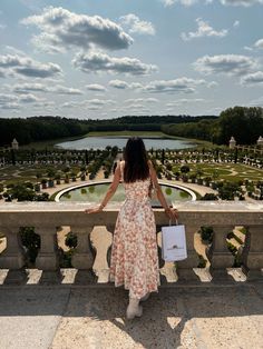 a woman in a dress standing on a balcony looking out over a formal garden area