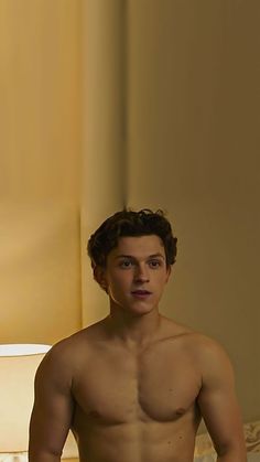 a shirtless young man sitting on top of a bed next to a white lamp