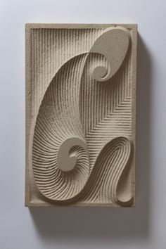 an abstract sculpture made out of concrete with swirls and circles on the top, against a white wall