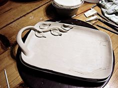 an old cast iron dish is sitting on a table next to paint brushes and other art supplies