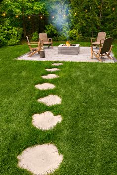 a fire pit in the middle of a grassy area with chairs and lights on it