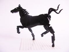 a black horse made out of legos on top of a white surface with one leg in the air