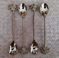 four spoons with palm trees on them sitting next to each other in front of a woven wall