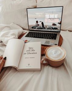 someone is reading a book and drinking coffee while using their laptop on the bed in front of them