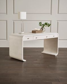 a white desk sitting on top of a hard wood floor next to a lamp and vase