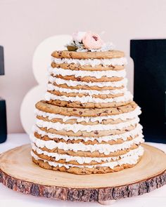 a tall cake with white frosting and flowers on top sitting on a wooden slice