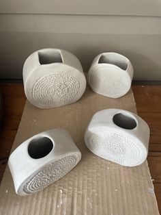 four white vases sitting on top of a cardboard covered floor next to a window