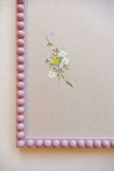 a pink frame with flowers painted on the side and beaded trim around the edge