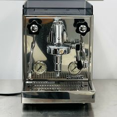 a silver coffee machine sitting on top of a counter next to a wall mounted clock