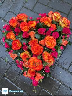 a heart shaped arrangement of orange and red roses on a brick sidewalk in the shape of a heart