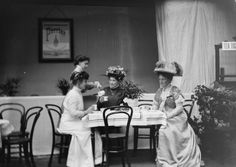 an old black and white photo of three women sitting at a table with flowers in their hair