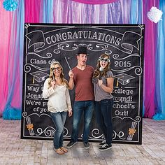 three people standing in front of a sign with congratulations written on it and balloons behind them