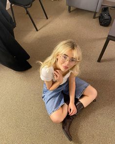 a woman sitting on the floor with her legs crossed and looking at the camera while wearing glasses