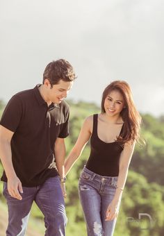 a young man and woman walking down a dirt road holding hands with trees in the background