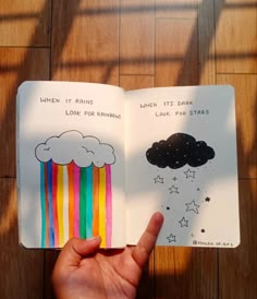 someone is holding an open book with rainbows and clouds