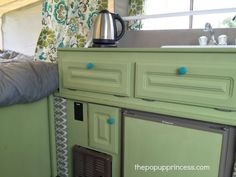 a green cabinet with blue knobs in a kitchen area next to a sink and window