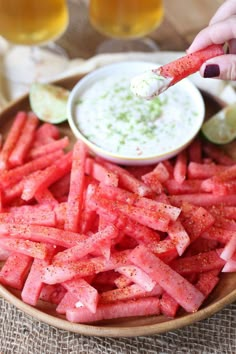 a person dipping some kind of sauce on top of watermelon sticks in a bowl