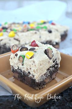 a brownie with white frosting and m & m candies on it sitting on a plate